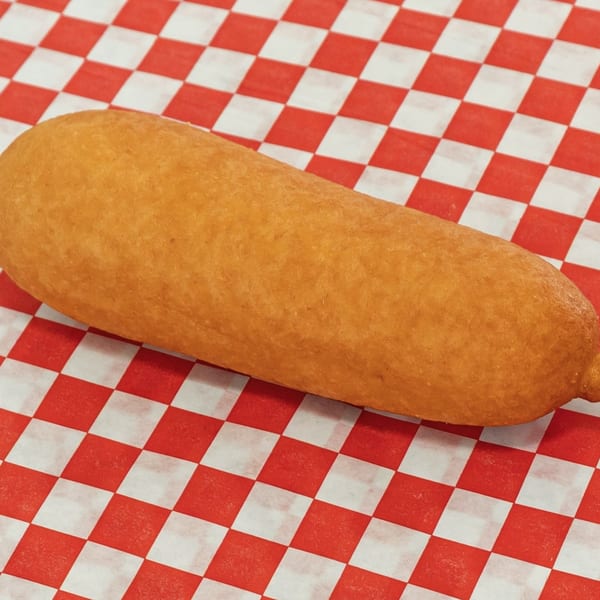 A golden-brown corn dog rests diagonally on a red and white checkered paper liner.