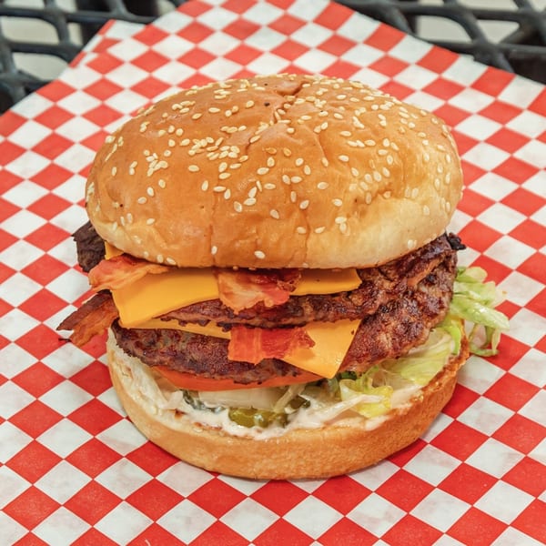 A double bacon cheeseburger from Nubbin's Drive-In, with lettuce, tomato, and sauce on checkered paper.