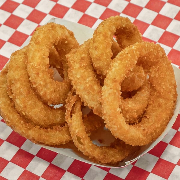 Golden-brown, crispy onion rings in a white paper tray on a red and white checkered surface.