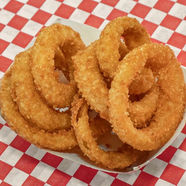Golden-brown, crispy onion rings in a white paper tray on a red and white checkered surface.