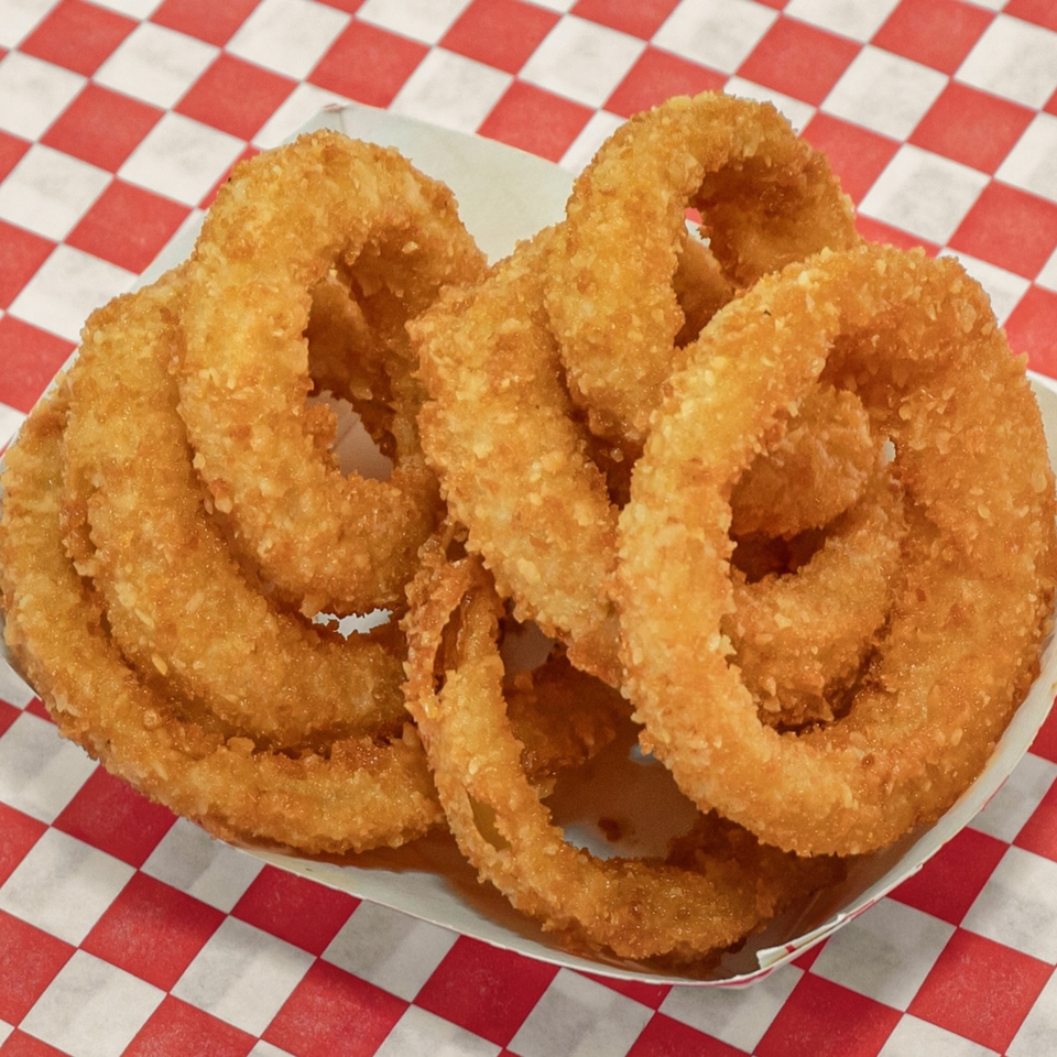 Golden-brown, crispy onion rings in a white paper tray on a red and white checkered surface.