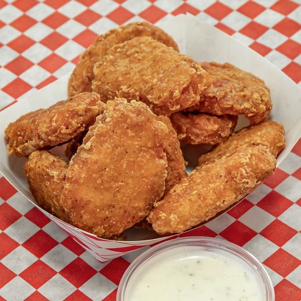 Crispy fried chicken nuggets in a paper tray with a side of dipping sauce on a red and white checkered surface.