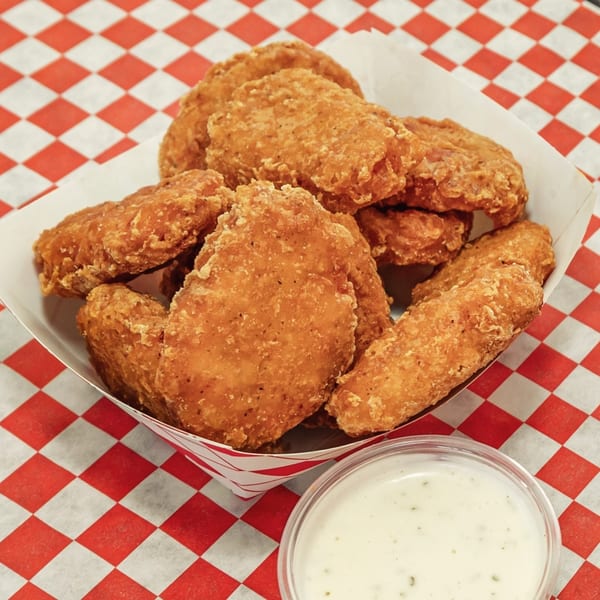 Crispy chicken nuggets in a paper tray with a side of ranch dressing on a red and white checkered surface.