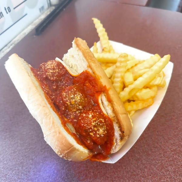 Meatball sub with marinara sauce and parmesan cheese, served with crinkle-cut fries.